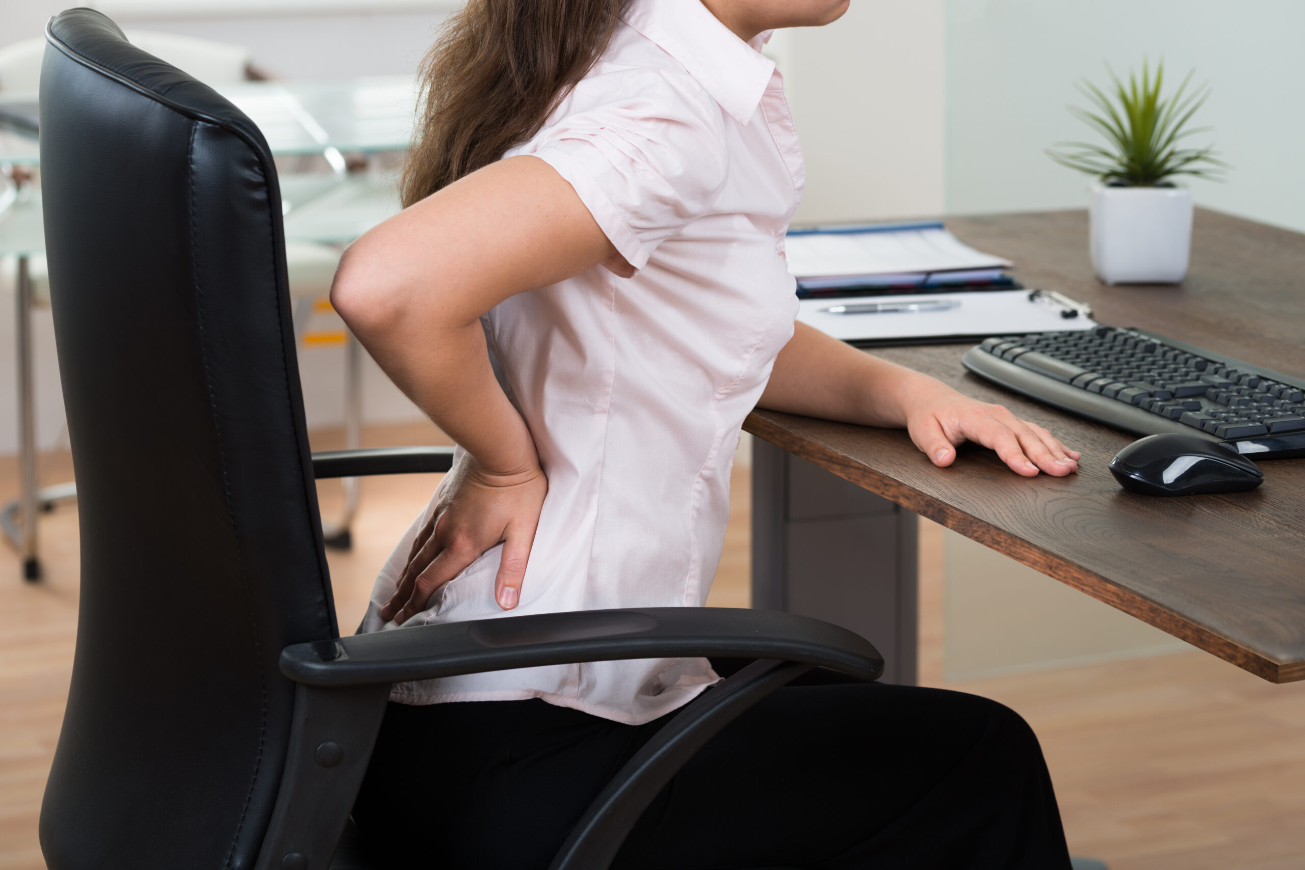 donna d'affari seduta alla scrivania con mal di schiena