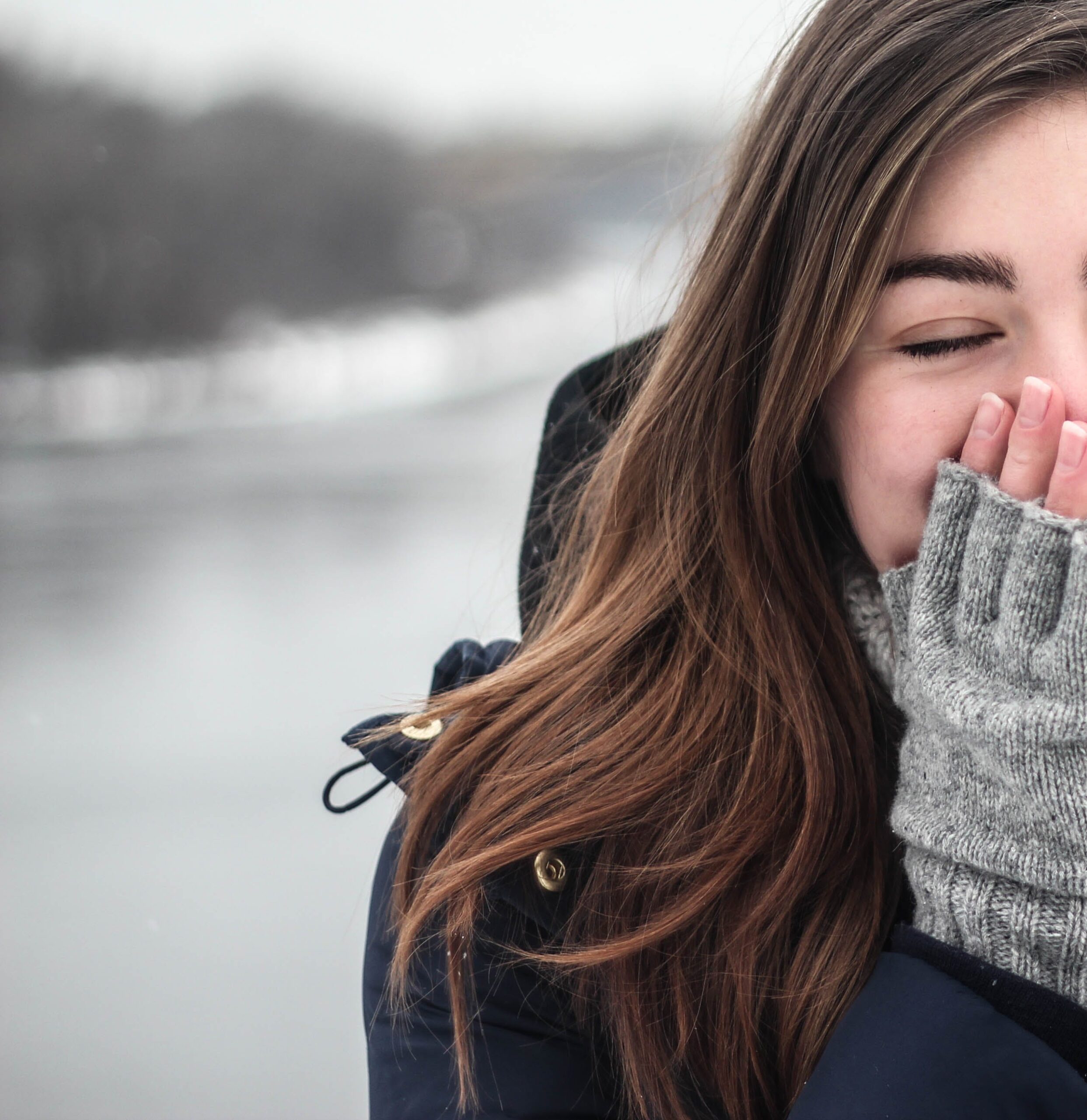 giovane donna vestita invernale con guanti forati sulle dita si riscalda le mani con la bocca